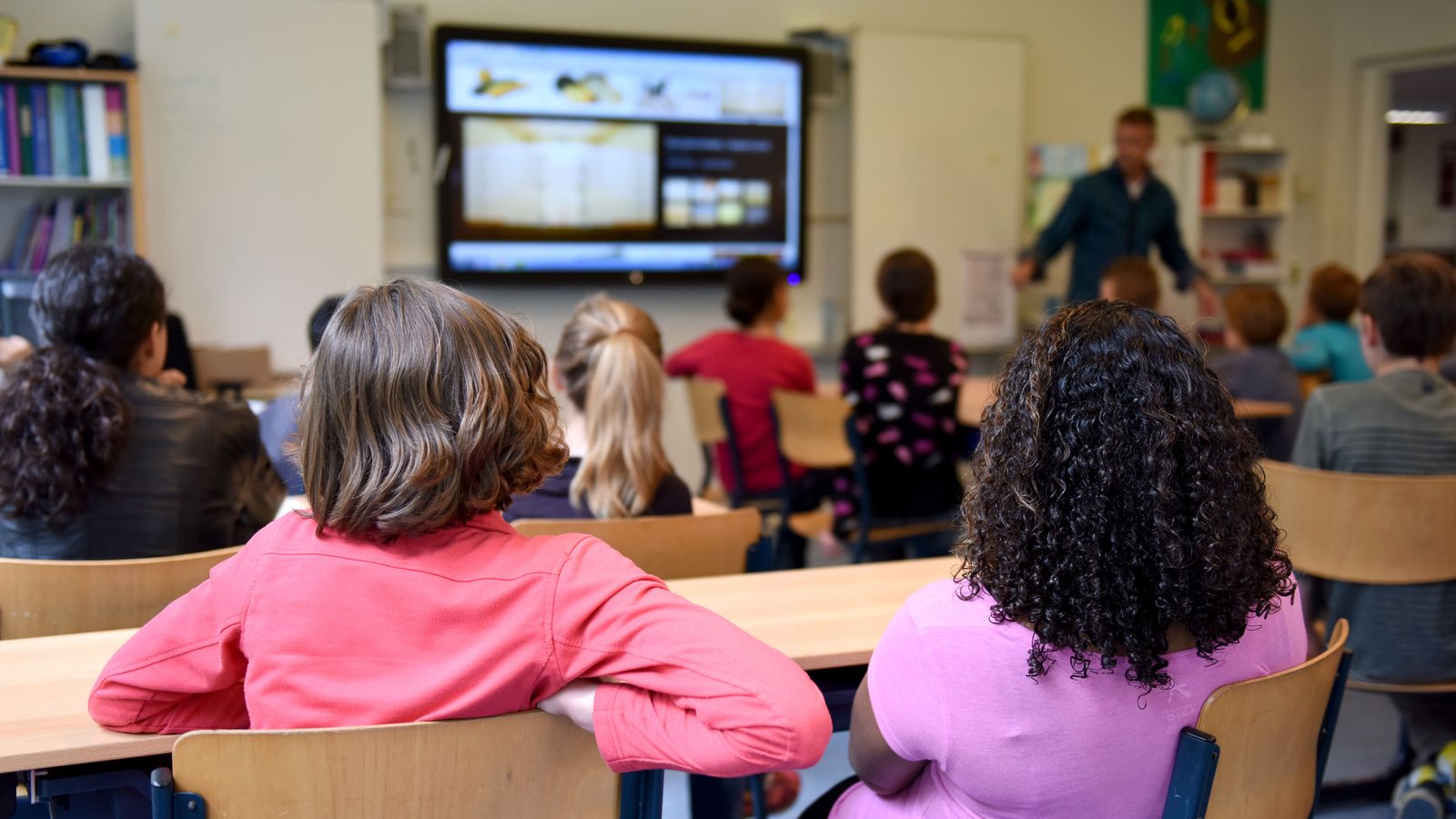 Des élèves suivent une leçon sur un tableau numérique dans une salle de classe colorée.